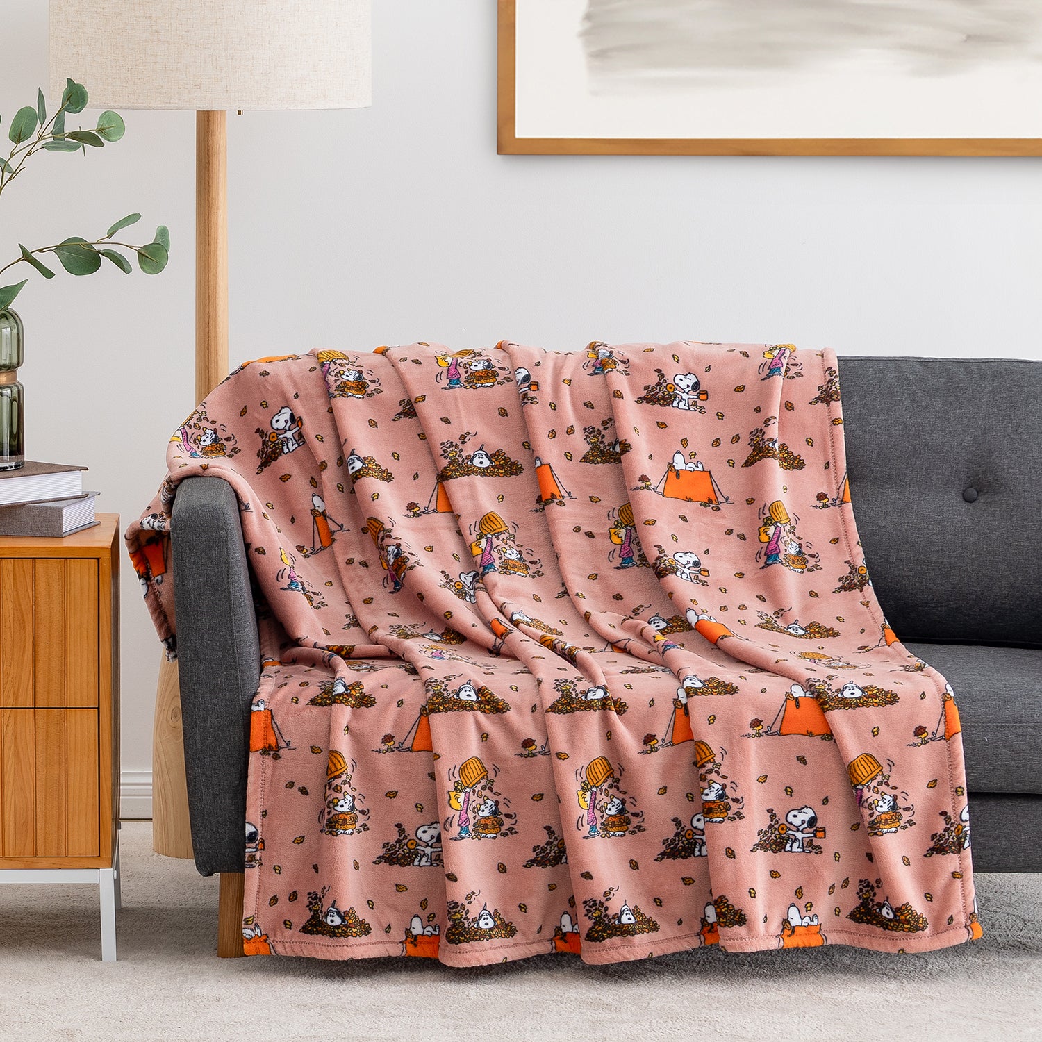 A pink fleece throw blanket with a cartoon camping pattern is draped over a gray sofa in a living room setting.