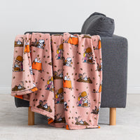 A pink fleece throw blanket with a cartoon character pattern draped over the back of a gray armchair in a living room setting.
