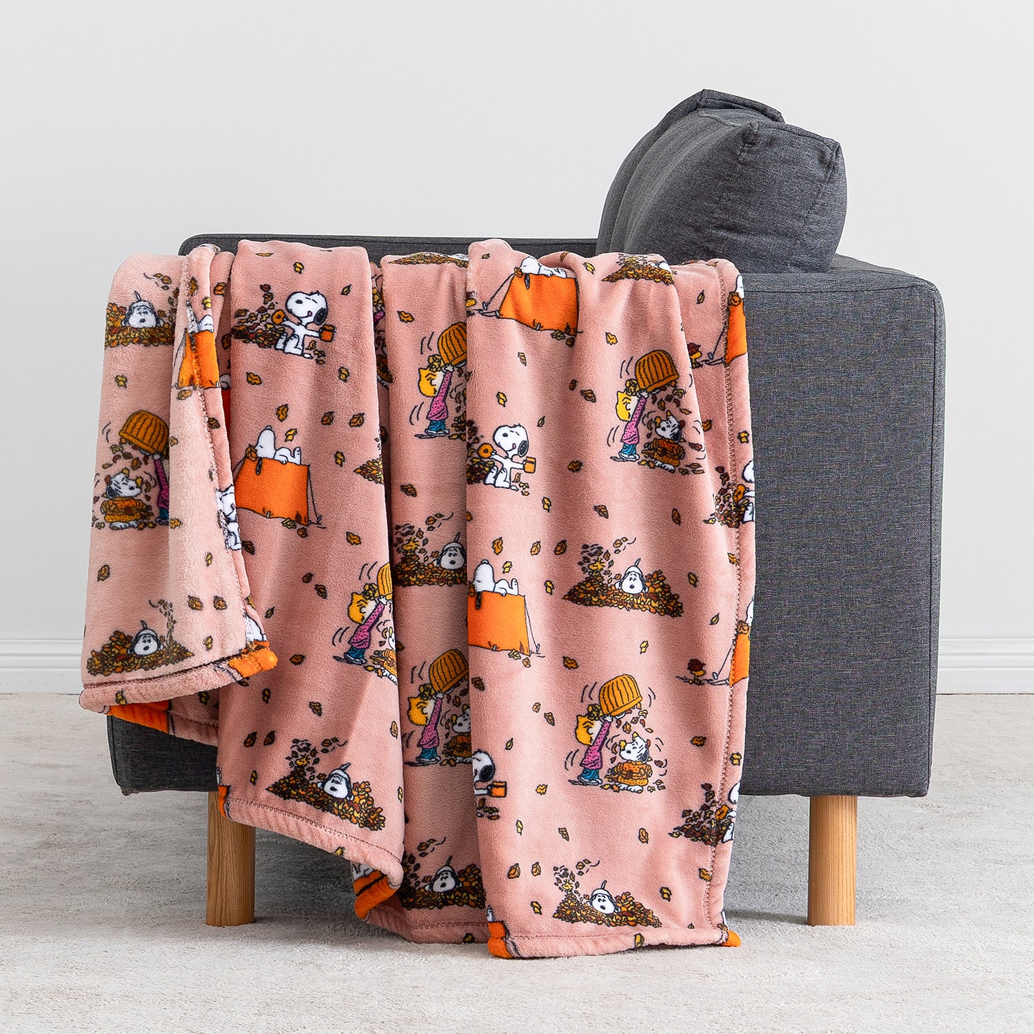 A pink fleece throw blanket with a cartoon character pattern draped over the back of a gray armchair in a living room setting.