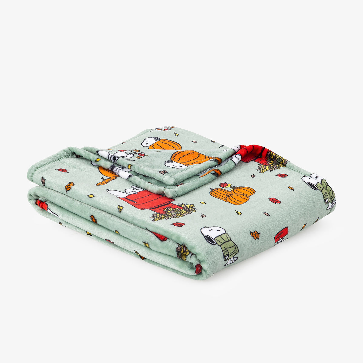 A folded plush blanket featuring a light mint green background with a repeating cartoon print of Snoopy and Woodstock in autumn outfits, including pumpkins, leaves, and red accents.