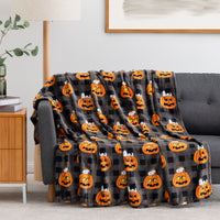 A dark gray and black plaid throw blanket with an orange jack-o'-lantern pattern is draped over a gray sofa in a living room setting.