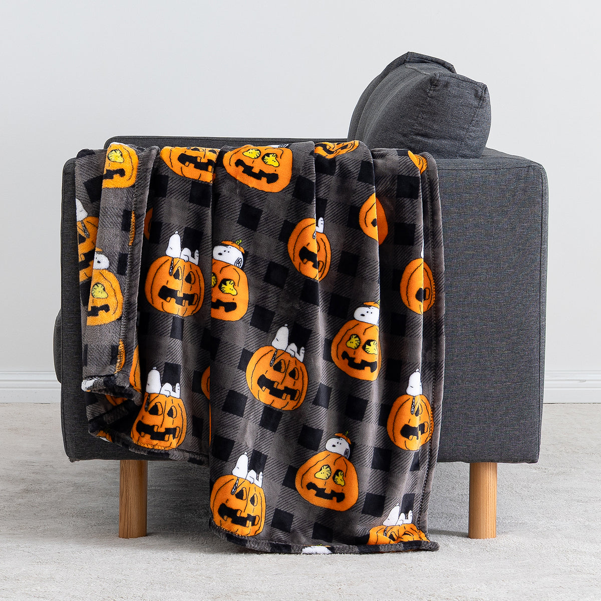 A gray throw blanket with an orange jack-o'-lantern and white ghost pattern draped over a dark gray armchair in a clean indoor setting.