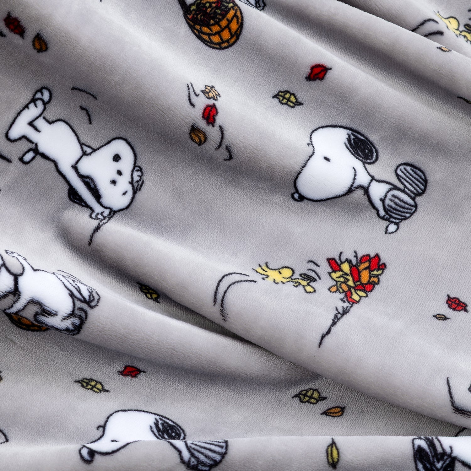 A close-up of a light gray fabric with a printed pattern of Snoopy and Woodstock in black and white, accented with small red, yellow, and brown autumn leaves.