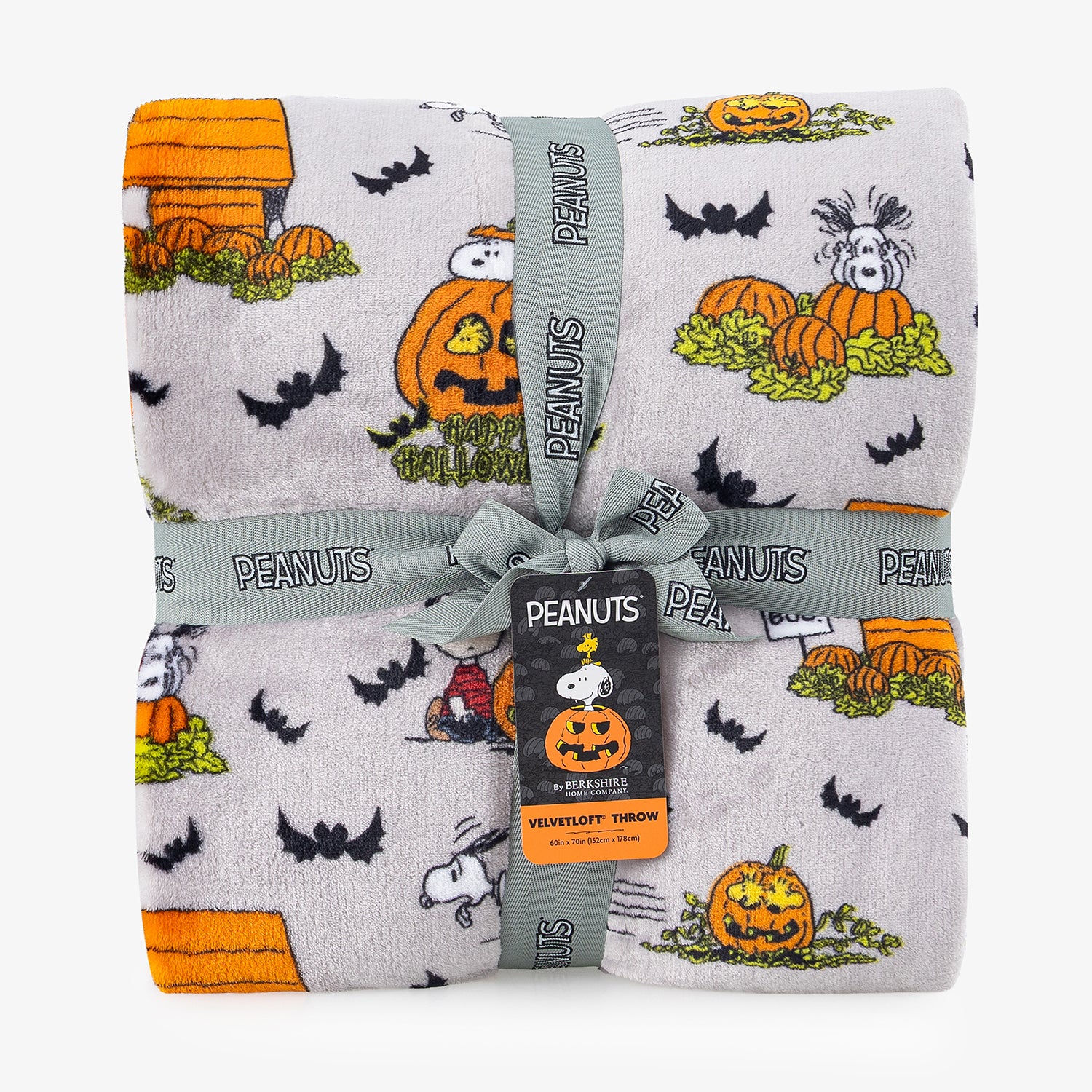 A folded plush throw blanket featuring a Peanuts Halloween print with Snoopy, Woodstock, pumpkins, bats, and a doghouse on a light gray background, wrapped with a gray ribbon and a Peanuts hangtag.