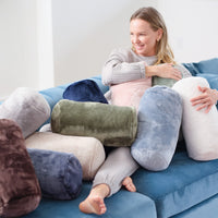 A woman sitting on a blue sofa with a variety of neckroll pillows.
