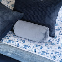 A blue neckroll pillow sitting on a bed with blue toned sheets and bedding.