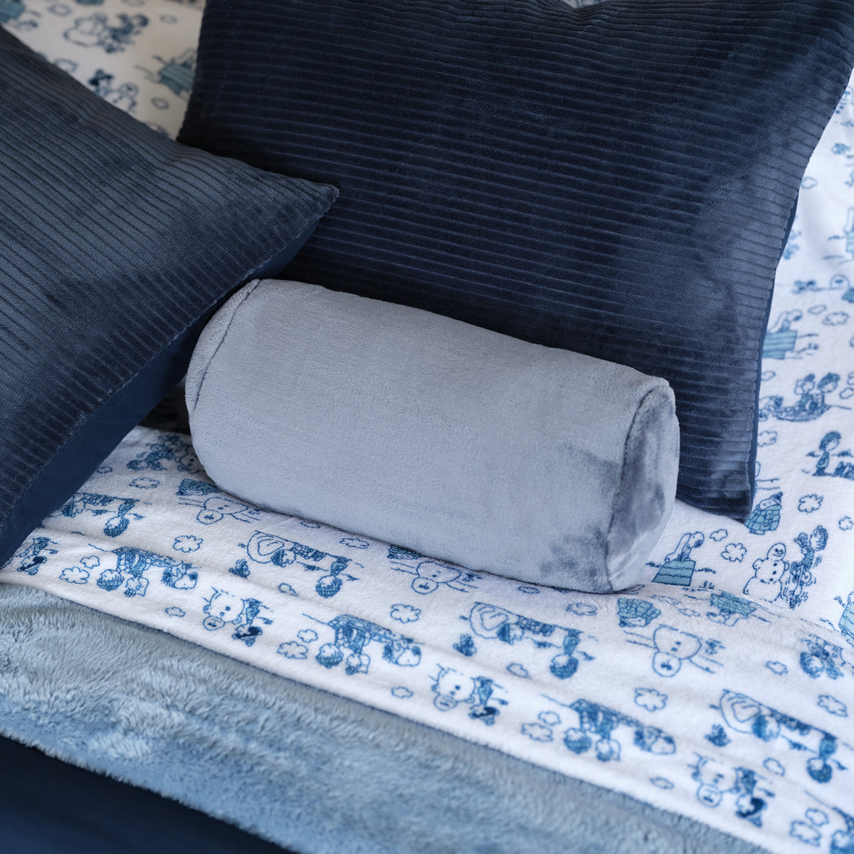 A blue neckroll pillow sitting on a bed with blue toned sheets and bedding.