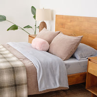 A decorated bed with neutral bedding and a pink neckroll pillow.