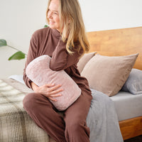 A woman sitting on a bed while holding a pink neckroll pillow.