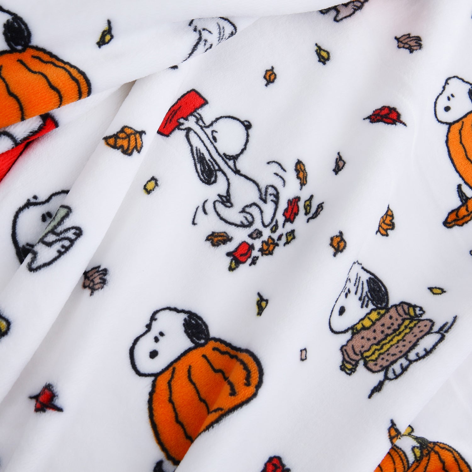 White fleece blanket featuring a repeating cartoon print of Snoopy in autumn costumes, including pumpkins, a red hat, and scattered orange and yellow leaves.