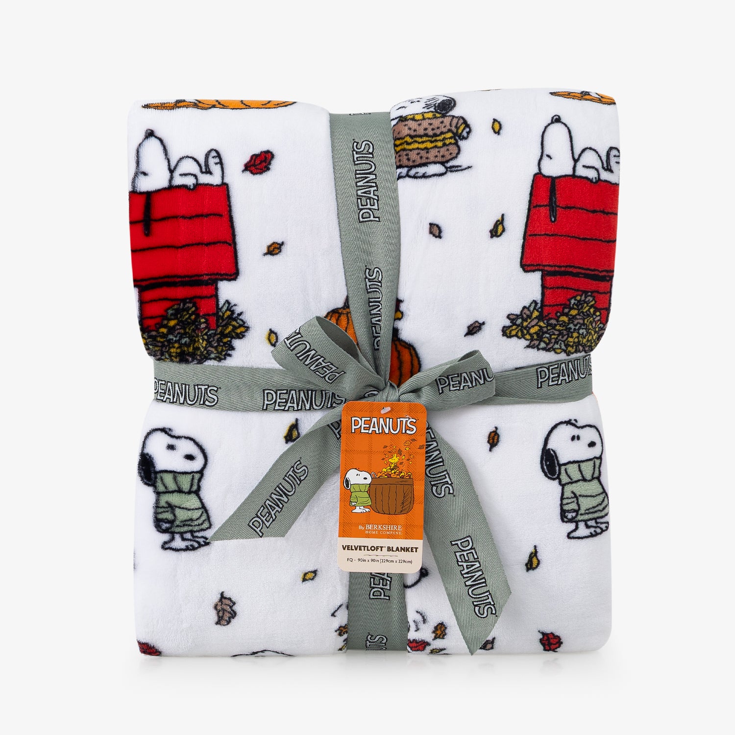 A folded white blanket with a repeating print of Snoopy and Woodstock in autumn-themed scenes, tied with a gray PEANUTS ribbon and a central orange tag.