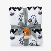 A white blanket with a black Snoopy and Woodstock pattern and zigzag border folded neatly on a white surface.
