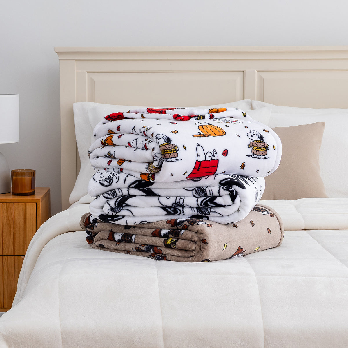 A stack of 3 printed Peanuts blankets folded on a bed.