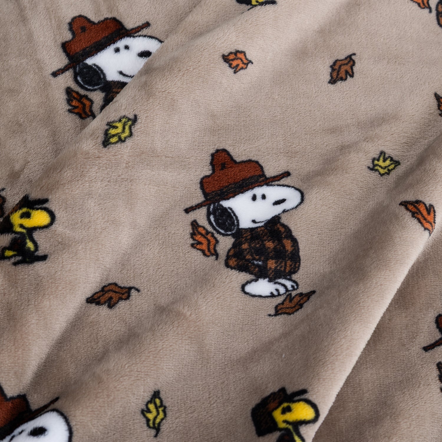 Close up of a tan peanuts printed blanket featuring snoopy in a jacket.
