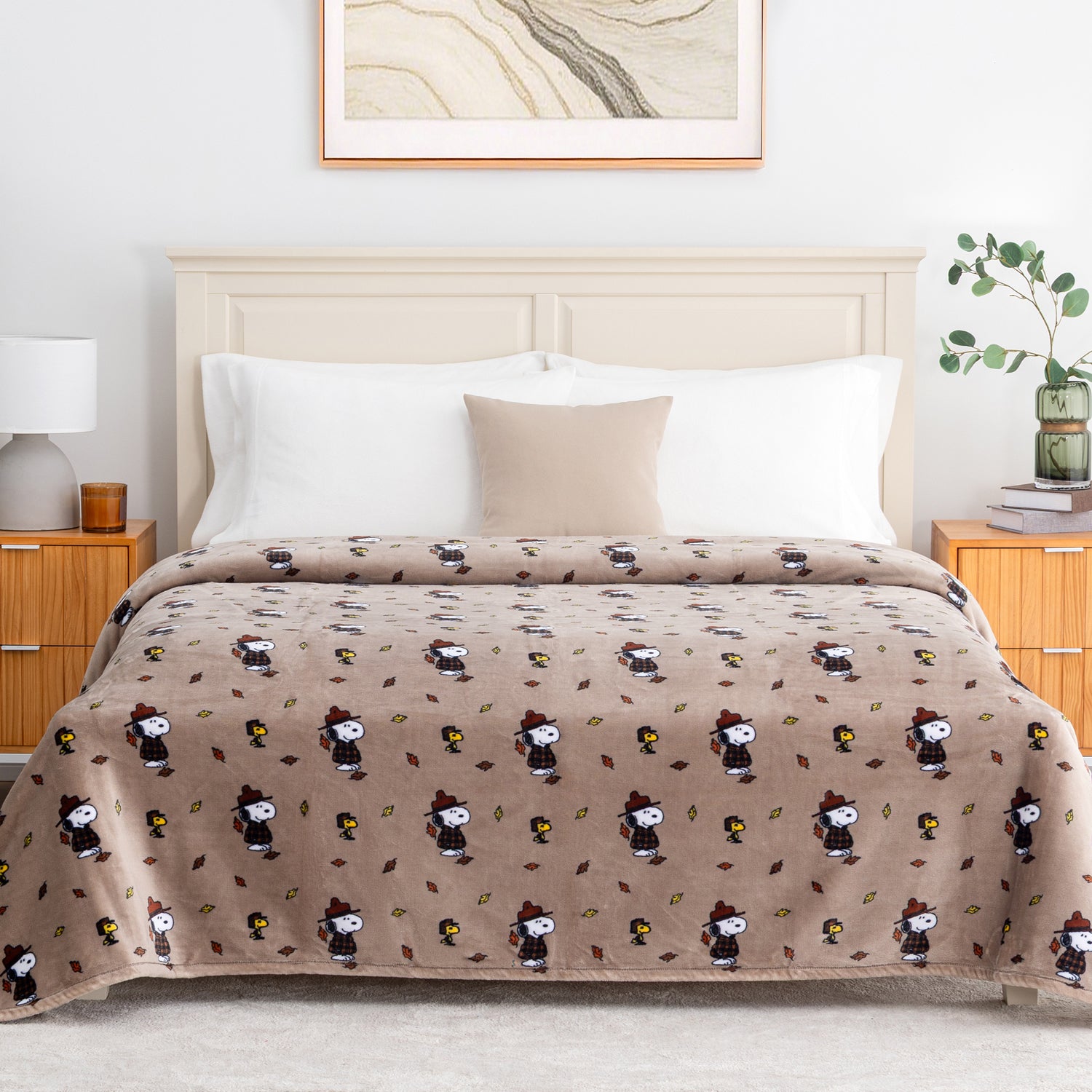A tan printed Peanuts blanket draped over a bed in a bright bedroom.