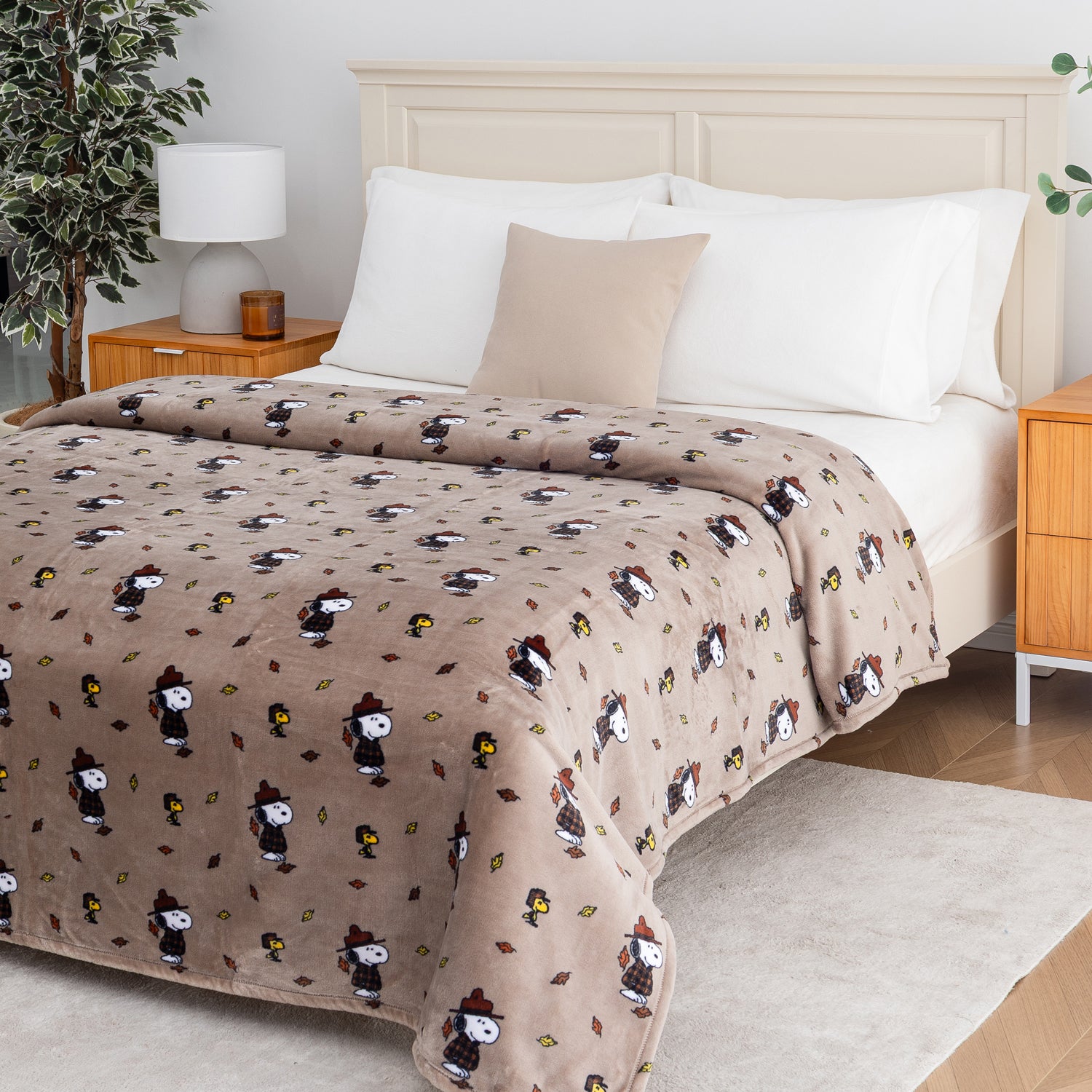 A cozy bed dressed in a plush beige blanket featuring a repeating print of cartoon characters in winter hats, styled in a bright, modern bedroom setting.
