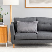 A grey heated lumbar pillow sitting on a grey sofa.
