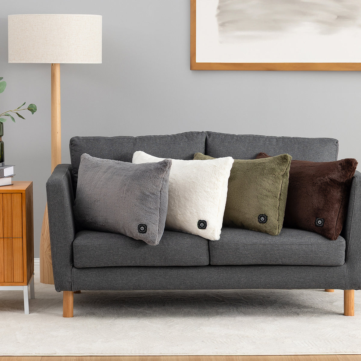 Four decorative throw pillows in gray, cream, olive green, and dark brown resting on a dark gray fabric sofa in a modern living room setting.