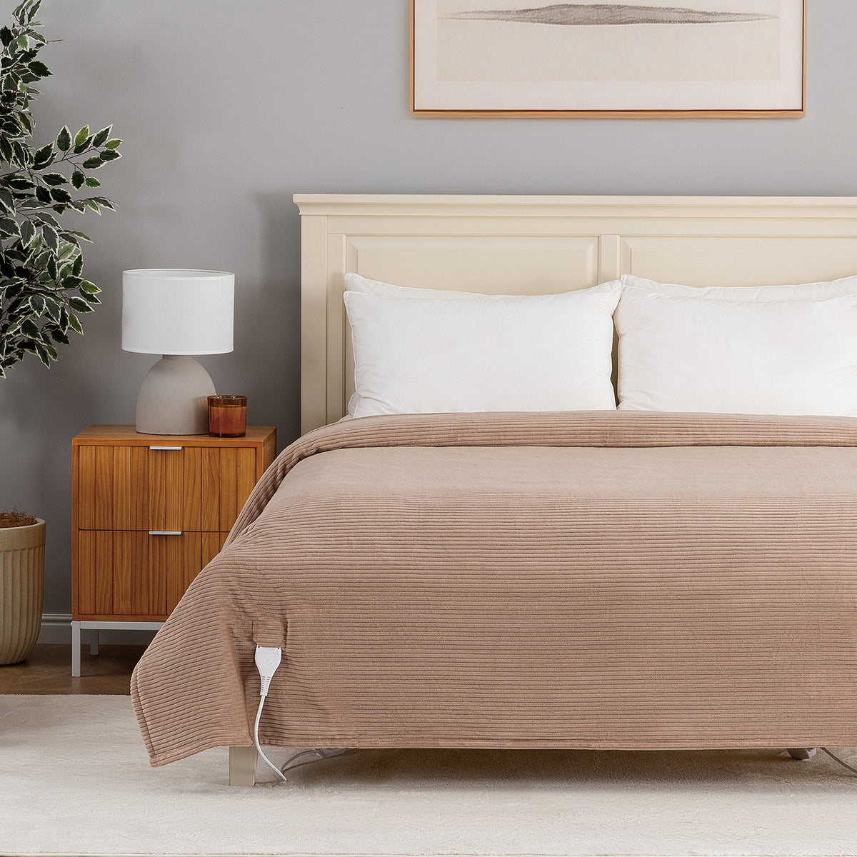 A bed dressed in a ribbed taupe-brown quilt or comforter, styled in a modern bedroom with a cream headboard, white pillows, a wooden nightstand, and a gray wall.