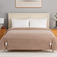A bed dressed in a ribbed taupe-brown quilted coverlet with two white pillows, set against a light wood headboard in a styled bedroom scene.