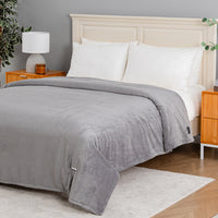 A gray ribbed fleece blanket with a matching gray striped duvet cover is neatly spread across a bed with white pillows and a cream-colored wooden headboard, set in a modern bedroom.