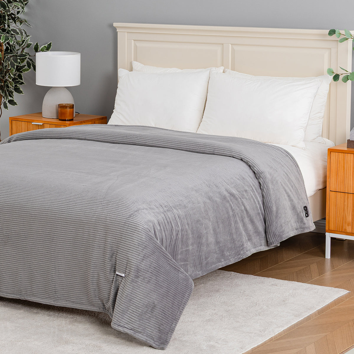 A gray ribbed fleece blanket with a matching gray striped duvet cover is neatly spread across a bed with white pillows and a cream-colored wooden headboard, set in a modern bedroom.
