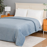 A light blue ribbed blanket is draped over a bed with white pillows and a cream headboard in a styled bedroom setting.