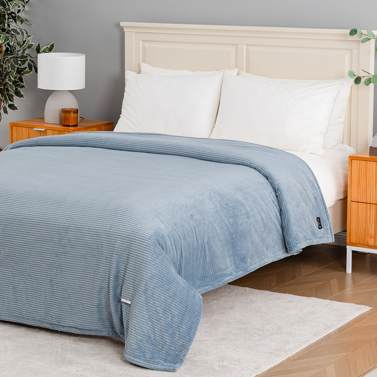 A light blue ribbed blanket is draped over a bed with white pillows and a cream headboard in a styled bedroom setting.