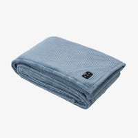 A folded light blue ribbed blanket with a small black control panel on the corner, shown on a clean white background.