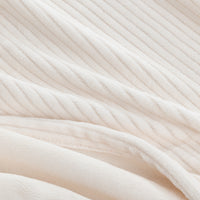 A close-up of a soft, cream-colored ribbed fabric, showing its plush texture and diagonal corduroy-like ridges.