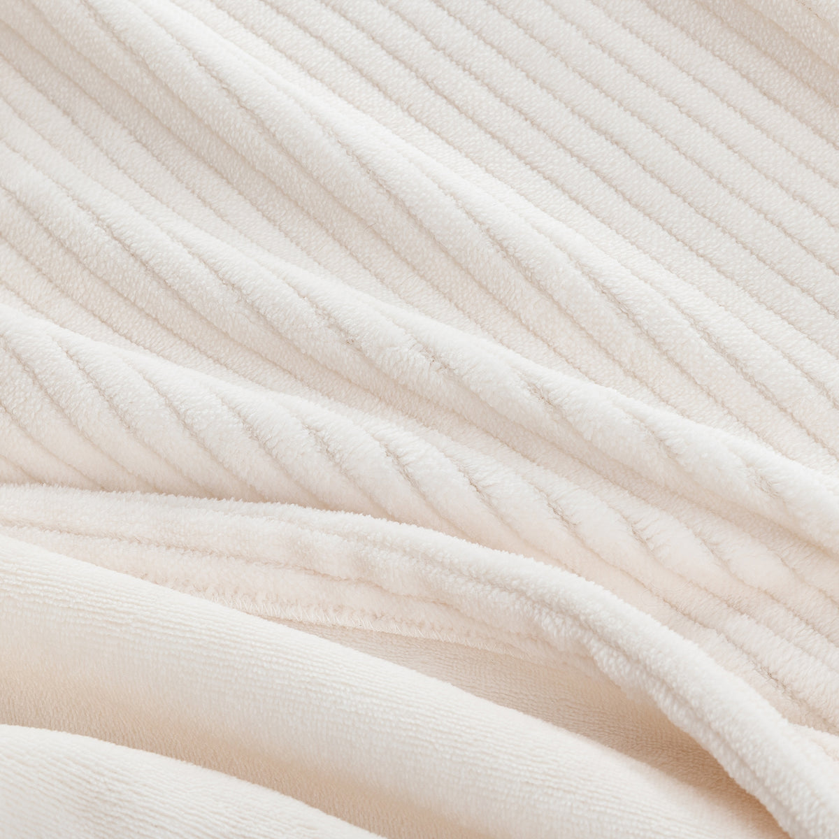 A close-up of a soft, cream-colored ribbed fabric, showing its plush texture and diagonal corduroy-like ridges.