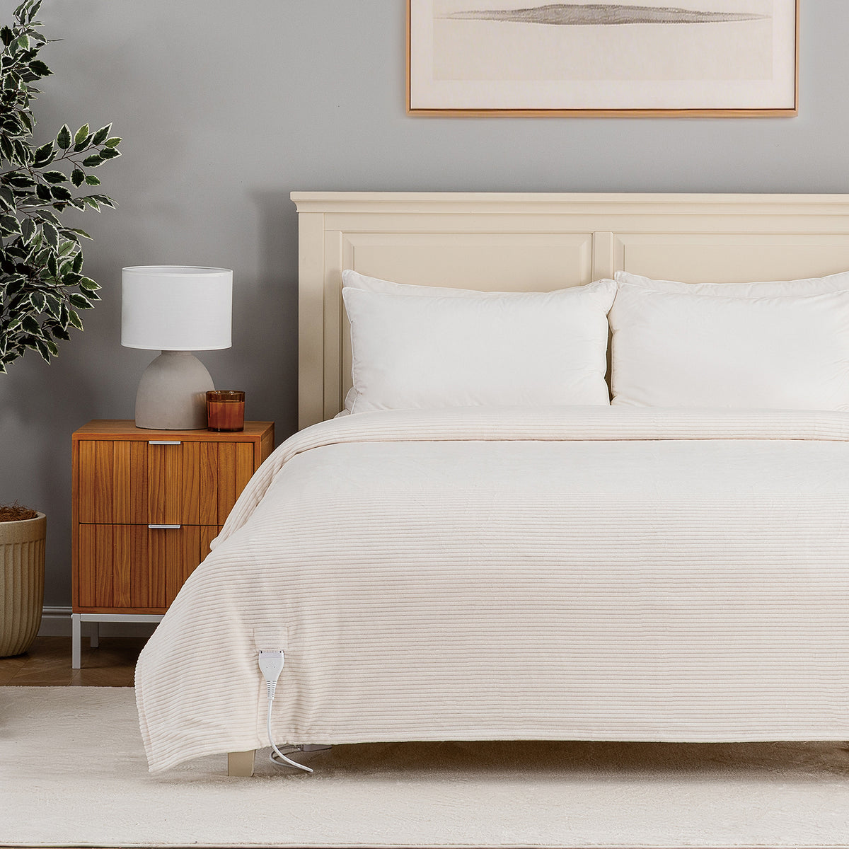 A bed dressed in a cream-colored ribbed duvet cover and white pillows, set in a styled bedroom with a wooden nightstand, lamp, and gray wall.