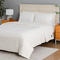 A neatly made bed with a white ribbed duvet cover and matching pillowcases, styled in a bedroom setting with a light wood headboard, bedside tables, a lamp, and a gray wall.