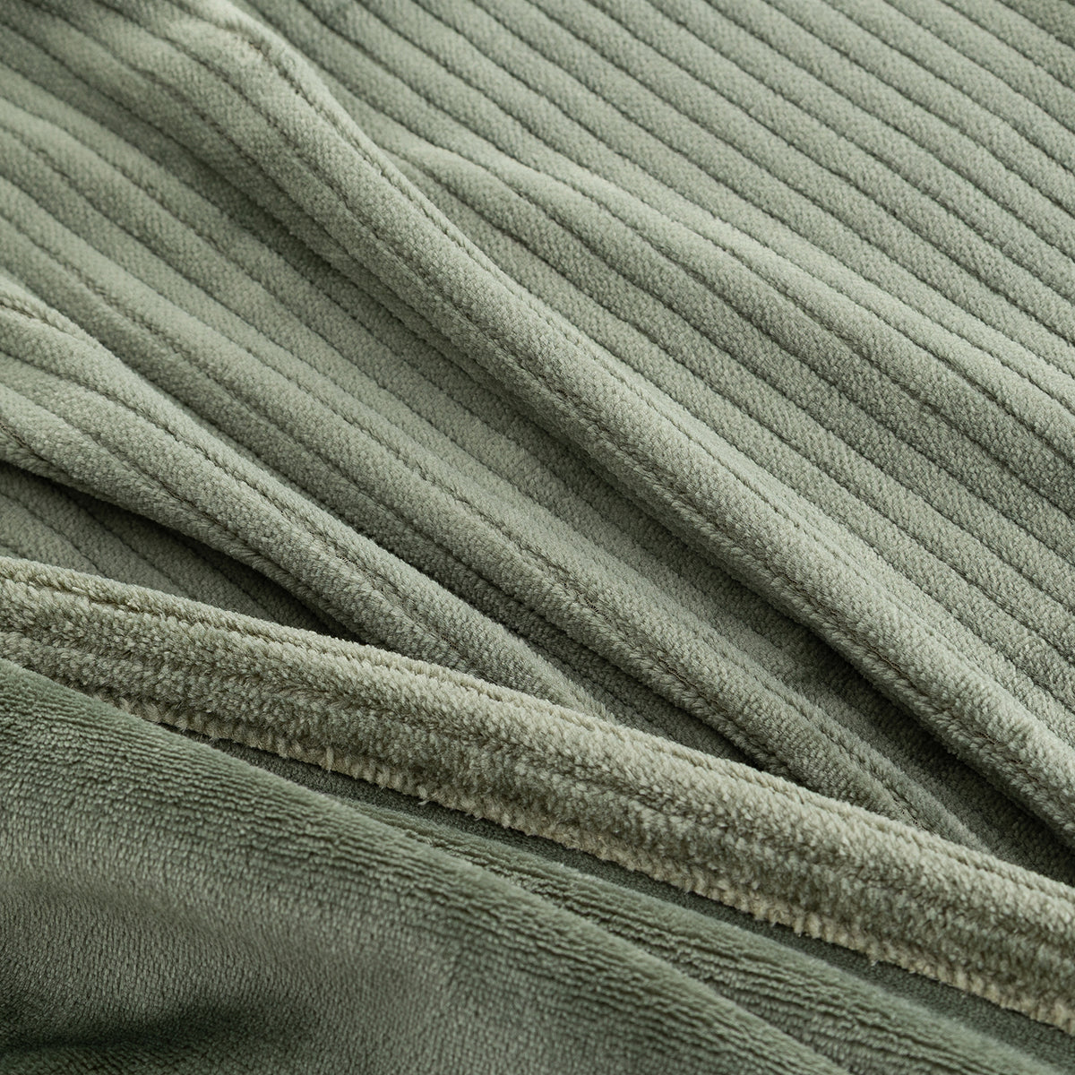 Close-up of a ribbed, plush fabric in a muted sage green color, showing the soft texture and folded drapery.
