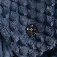 Close-up of a dark blue textured fleece blanket with a black remote control resting on top, showing the remote's power and mode buttons.