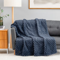 A textured navy blue throw blanket with a raised diamond pattern draped over a gray sofa in a modern living room setting.