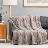 A grey textured faux fur heated throw draped over a chair.