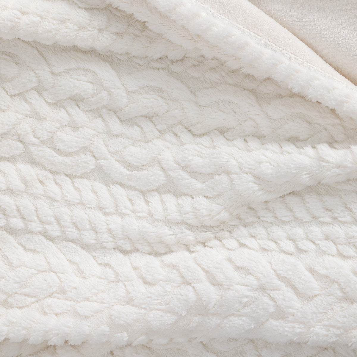 Close-up of a soft, textured white sherpa or fleece blanket with a raised cable-knit pattern on the top side and a smooth cream underside.