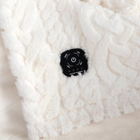Close-up of a white cable-knit heated blanket with a black control patch showing temperature and power settings.