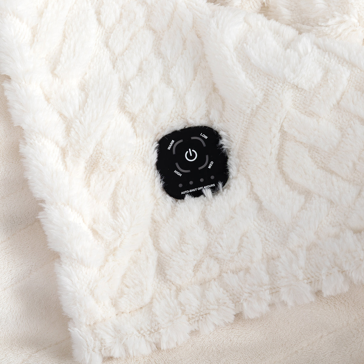 Close-up of a white cable-knit heated blanket with a black control patch showing temperature and power settings.