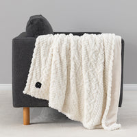 Cream colored faux fur heated throw draped over a chair.