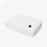 Cream colored faux fur heated throw folded neatly on a white surface.