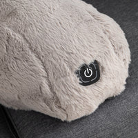 Close-up of a fluffy light gray heated massage pillow with a black power button on a dark gray fabric surface.