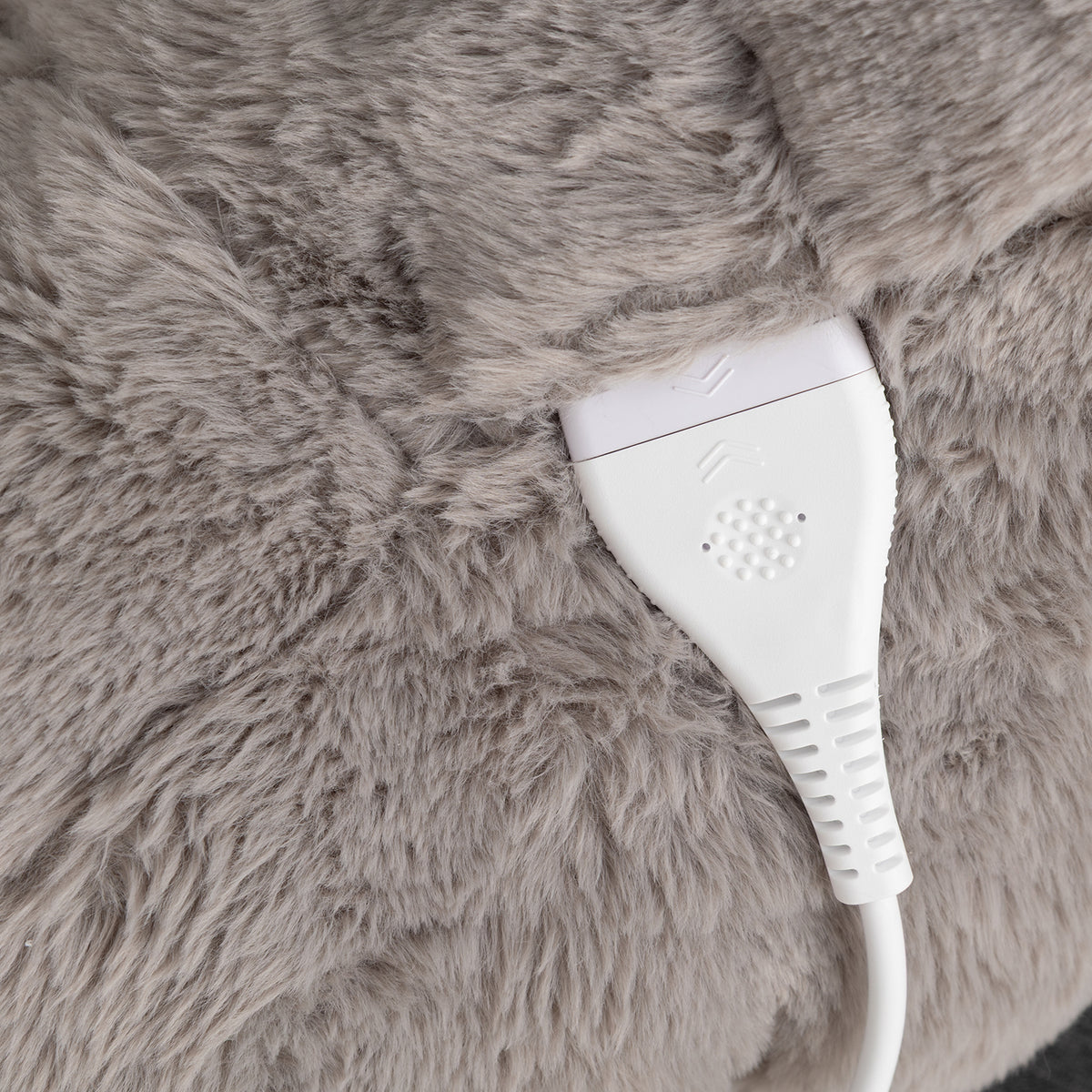 Close-up of a plush gray faux-fur surface with a white power cord and plug inserted.