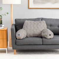 A gray textured lumbar pillow with two cylindrical bolster arms rests on a dark gray sofa in a modern living room setting.