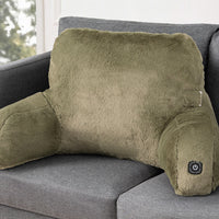 An olive green plush heated corner support pillow resting on a gray fabric sofa, with a small power button visible on the lower right armrest.