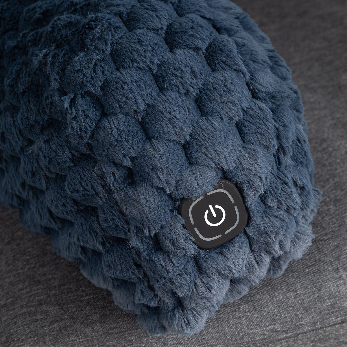 Close-up of a dark blue textured, chunky boucle fabric item with a black power button on a gray fabric surface.
