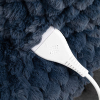 Close-up of a white electronic control module connected to a thick white cable, set against a dark navy blue textured faux fur surface.