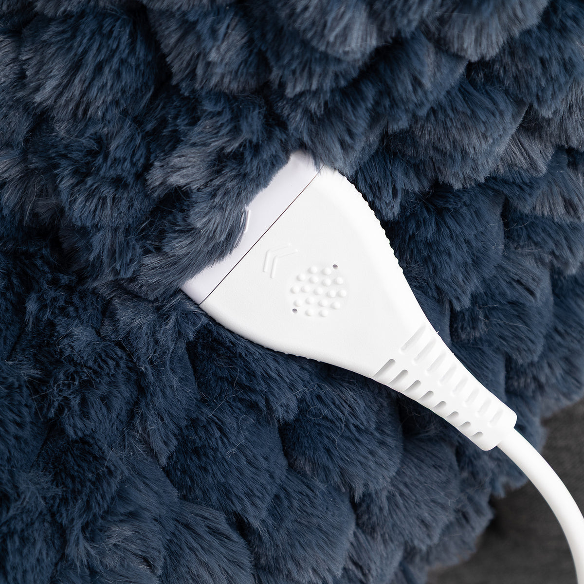 Close-up of a white electronic control module connected to a thick white cable, set against a dark navy blue textured faux fur surface.
