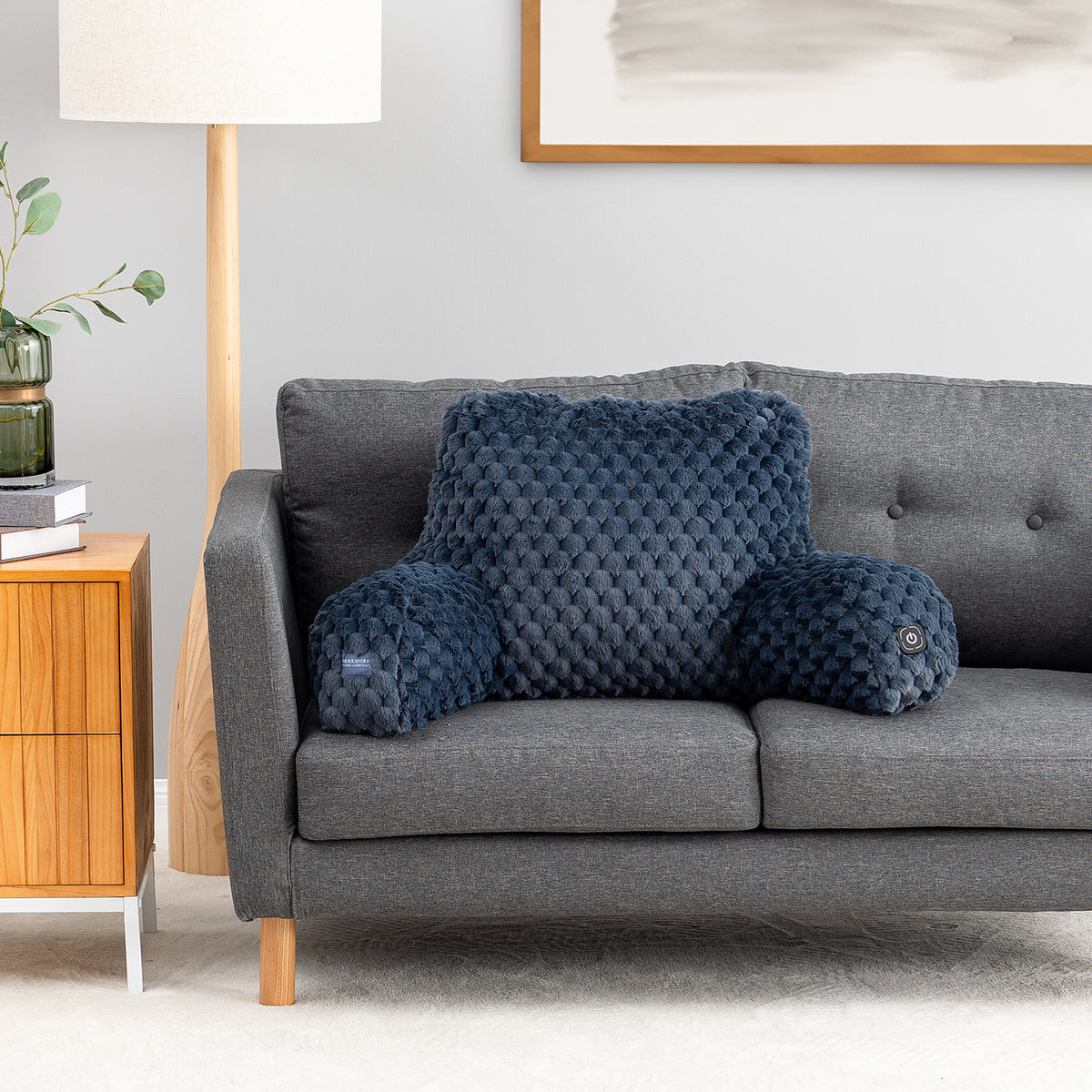A dark blue quilted lumbar pillow and matching cylindrical bolster pillows displayed on a gray fabric sofa in a modern living room setting.